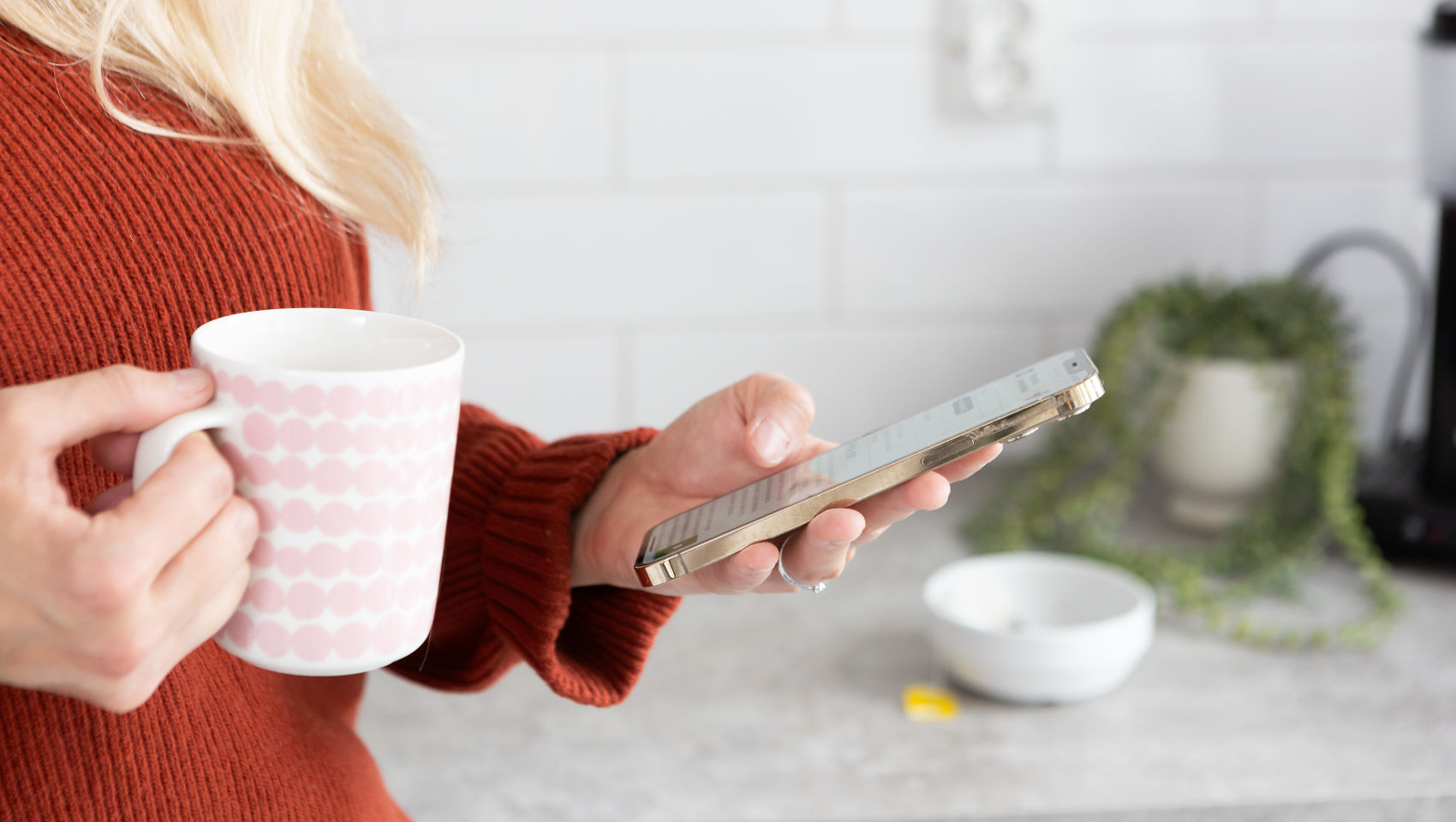 Nainen tarkastelee puhelinta kahvikuppi kädessä